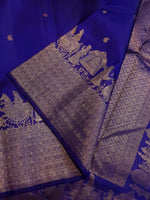Load image into Gallery viewer, A royal blue silk saree with intricate gold zari Banarasi motifs, featuring a heavily patterned border and a draped pallu.

