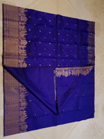 Load image into Gallery viewer, A royal blue silk saree with intricate gold zari borders and small gold motifs, laid flat on a light beige patterned tile floor.
