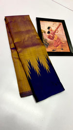 Load image into Gallery viewer, A folded traditional Indian saree displayed on a white surface next to a framed painting of a musician. The saree features a golden-yellow body with a deep navy blue border decorated with a jagged ikat pattern.
